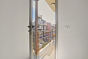 Vista desde un balcón con puerta de vidrio, baranda de metal y una pequeña mesa con una silla.