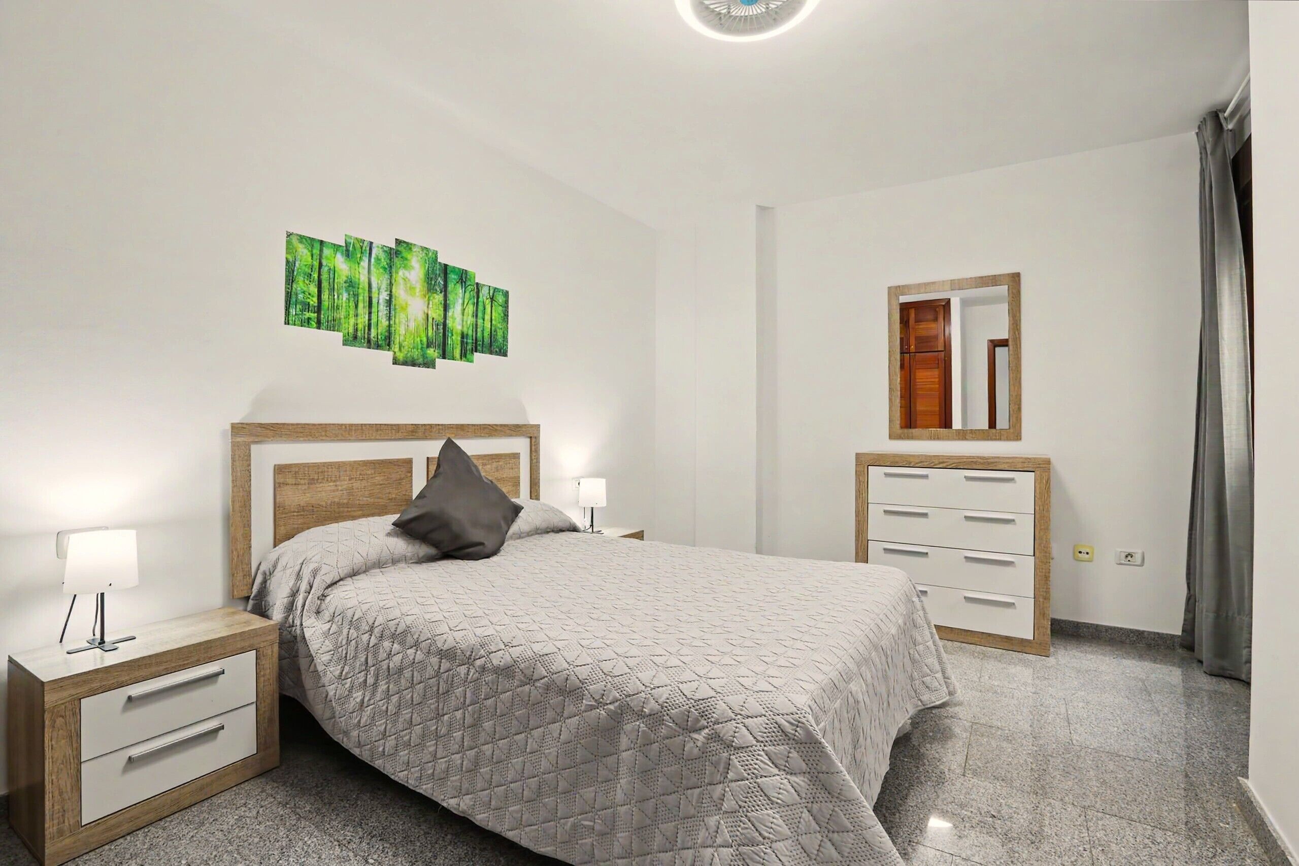 Une chambre à coucher comprenant un lit, des tables de chevet, une commode, un miroir et une  œuvre d’art murale.