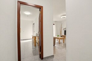 Un passadís amb una porta de fusta, una zona de dinar amb taula i cadires, i un mirall que reflecteix l'espai.