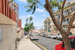 Una calle bordeada de coches aparcados, aceras y edificios de varios pisos con balcones.