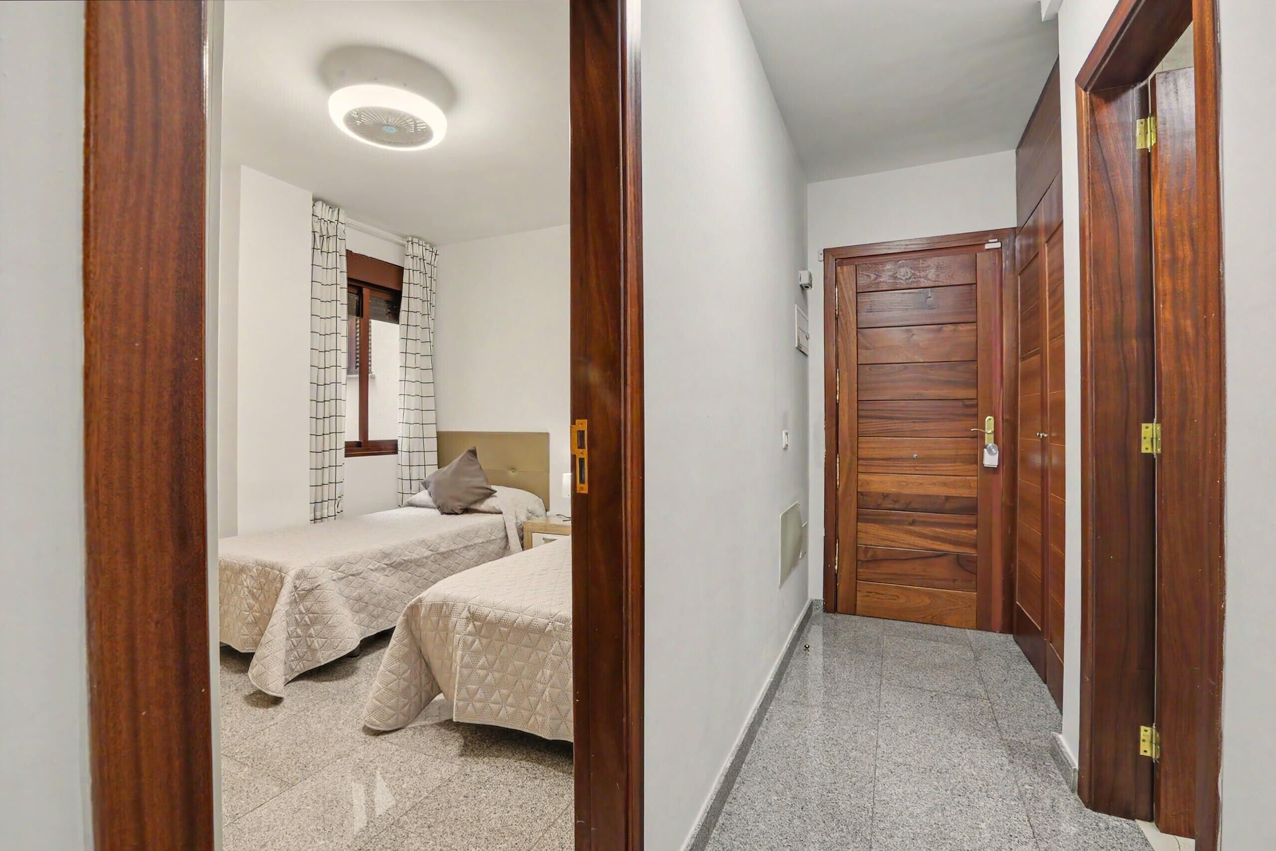 Een hotelkamer met twee bedden, een houten garderobe, een spiegel en een plafondlamp.