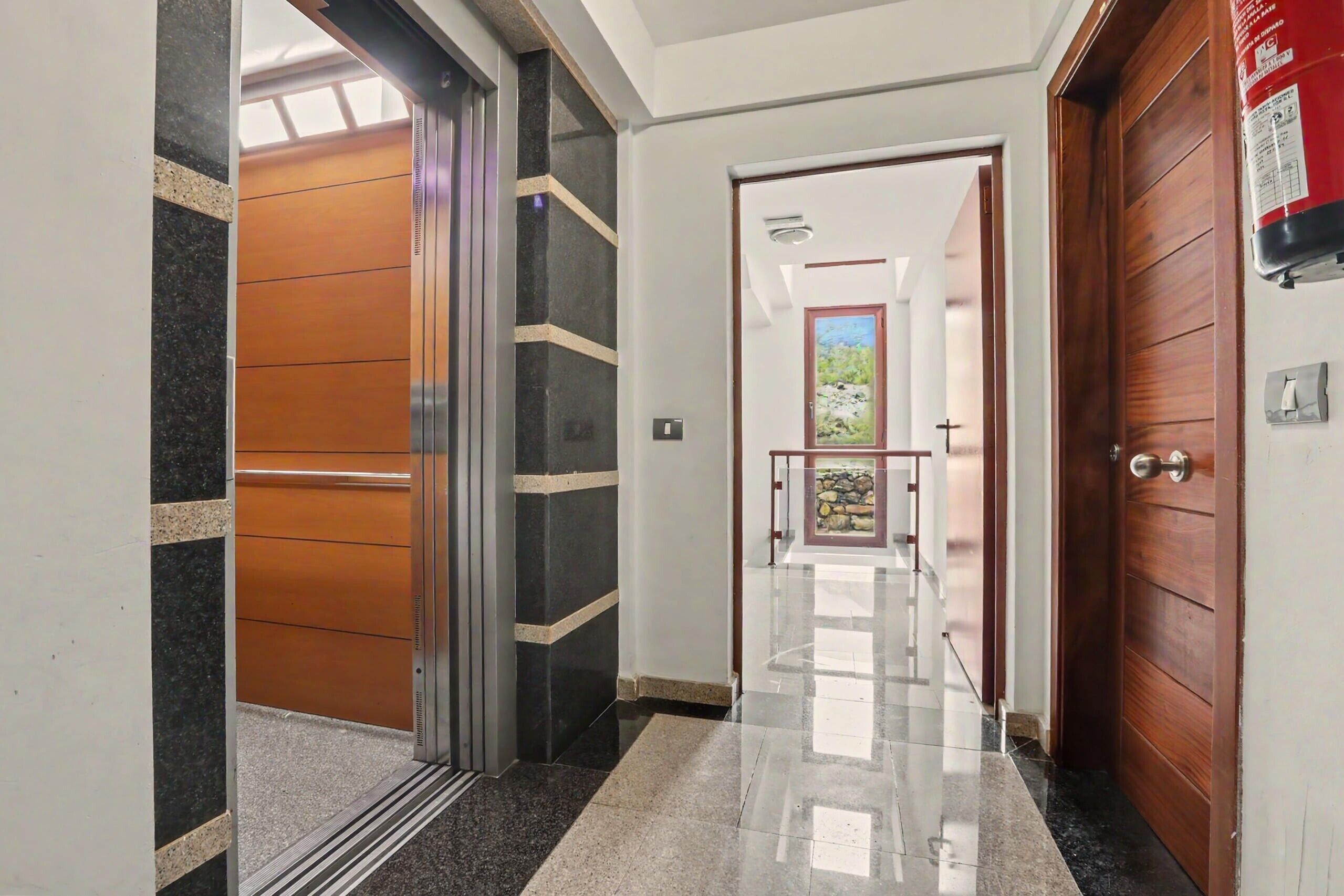 Un pasillo con piso pulido, una puerta de madera y vista a una habitación con ventana.