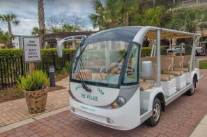 Un tramway de plage arborant le logo « The Village », doté de sièges pour les passagers et d’un panneau indiquant le service de stationnement pour les visiteurs de la plage.