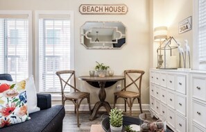 Une pièce comprenant une table à manger, deux chaises, un canapé, un meuble et une pancarte indiquant « MAISON DE PLAGE ».