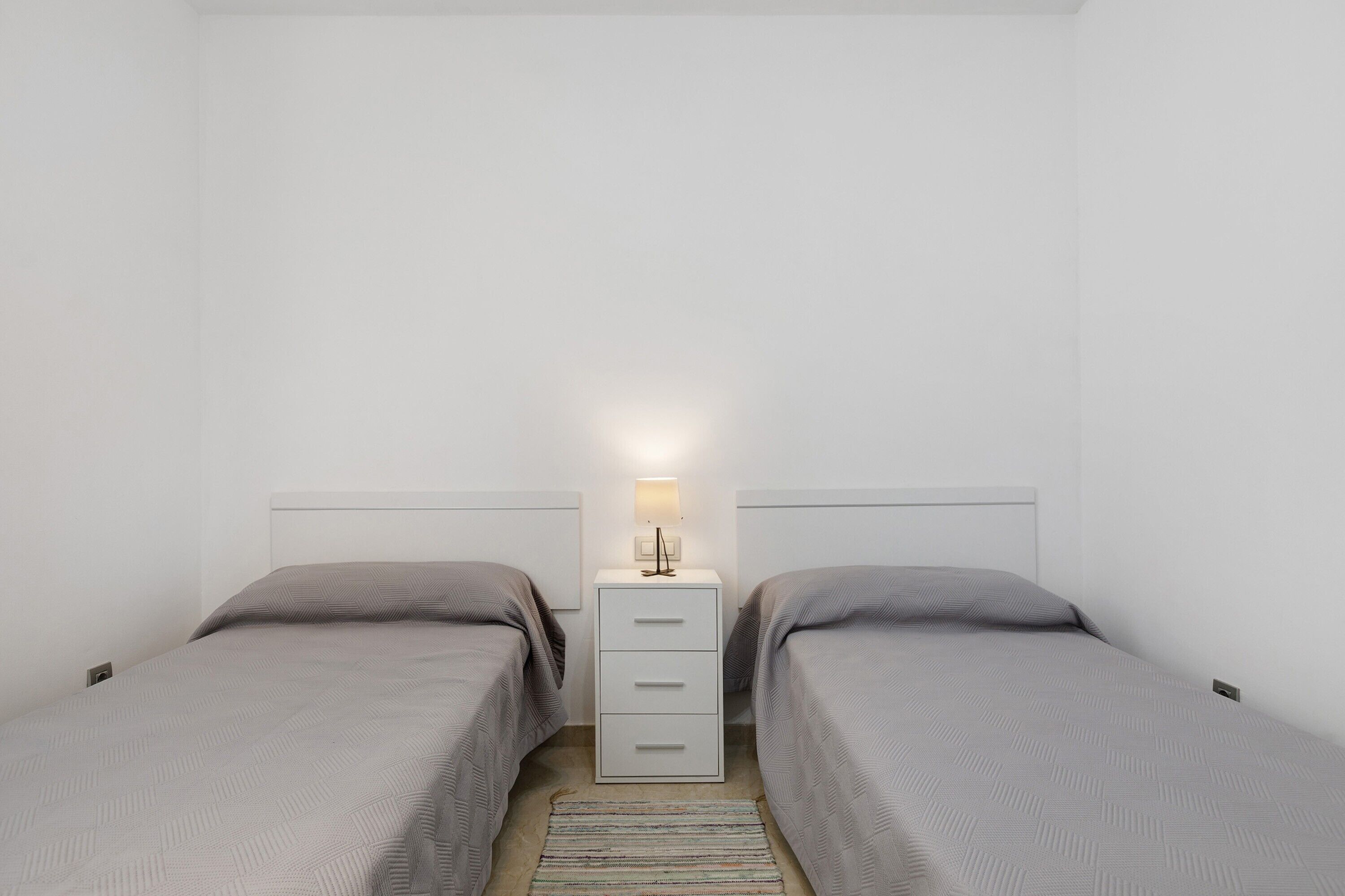 Habitación doble con dos camas, una mesita de noche y una lámpara.