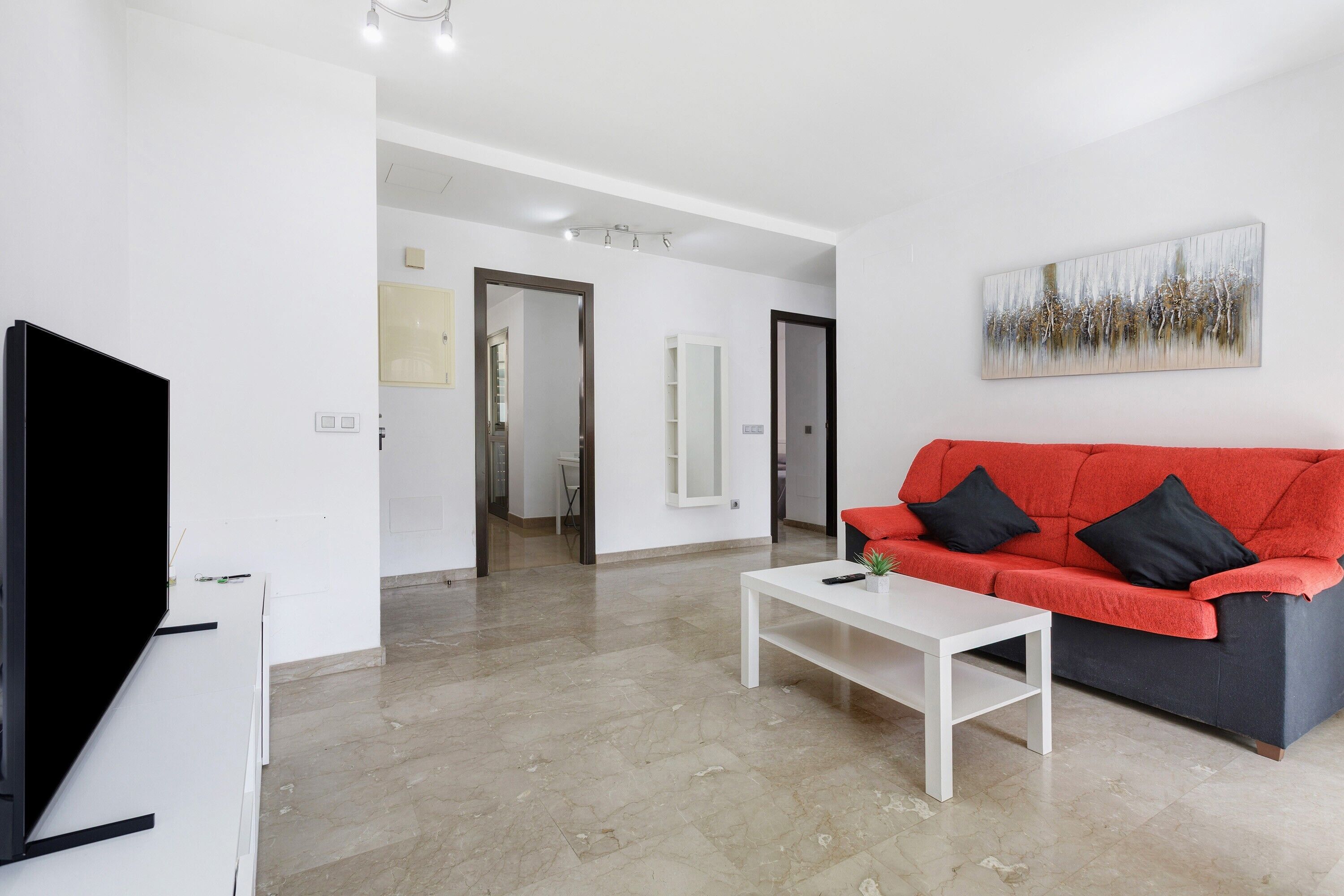 A modern living room with a red sofa, a white coffee table, and a flat-screen TV.