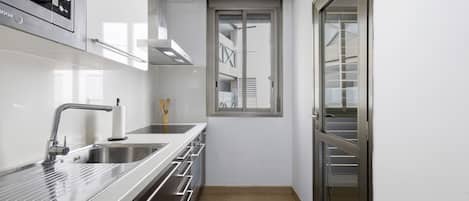 Una cocina estrecha con electrodomésticos de acero inoxidable, horno empotrado y ventana con vista a un edificio.