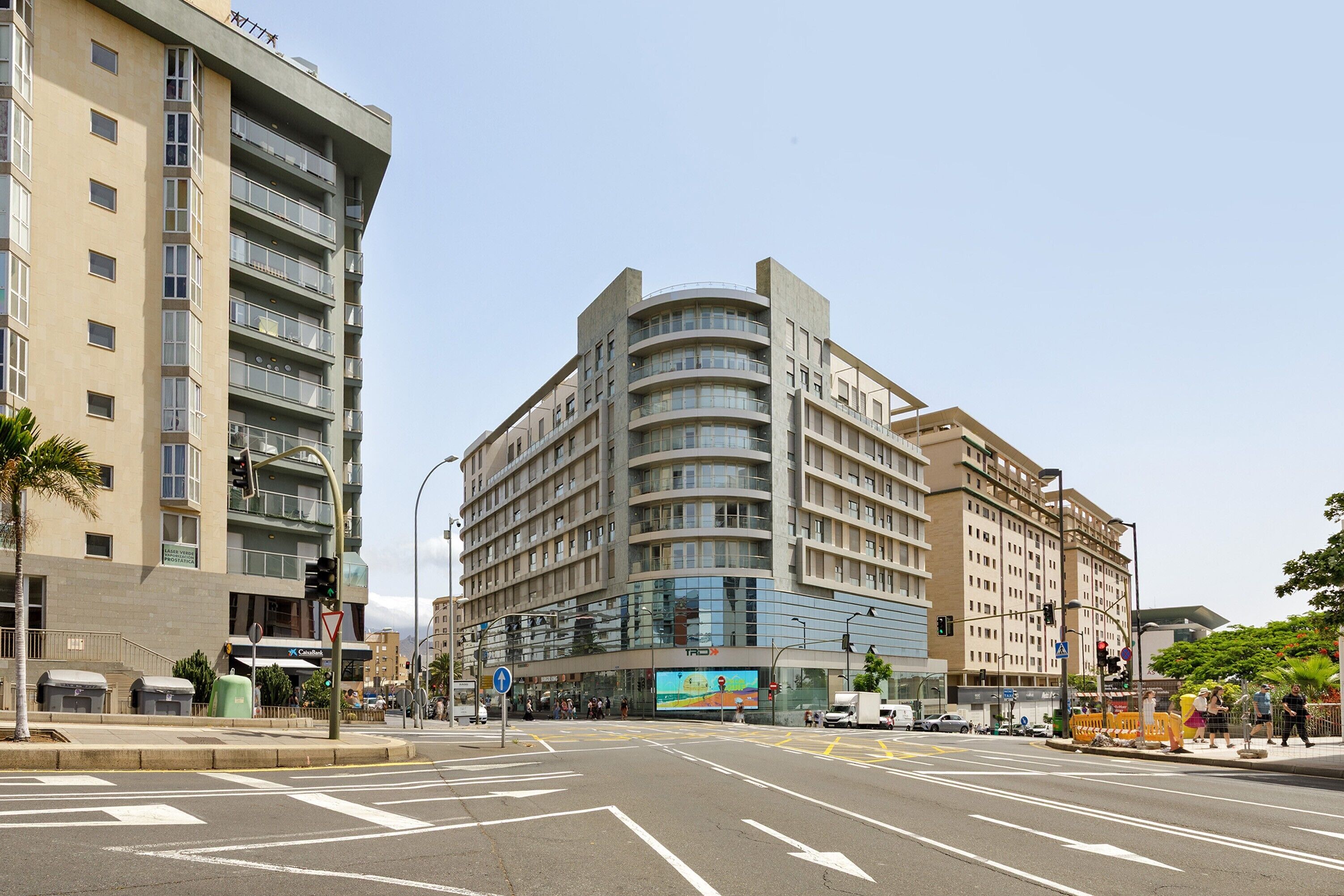 Un edificio de varios pisos con fachada curva, entrada visible y paso de peatones.