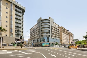 A multi-story building with a curved facade, a visible entrance, and a pedestrian crossing. - NG Zenith - Santa Cruz de Tenerife (Santa Cruz de Tenerife)
