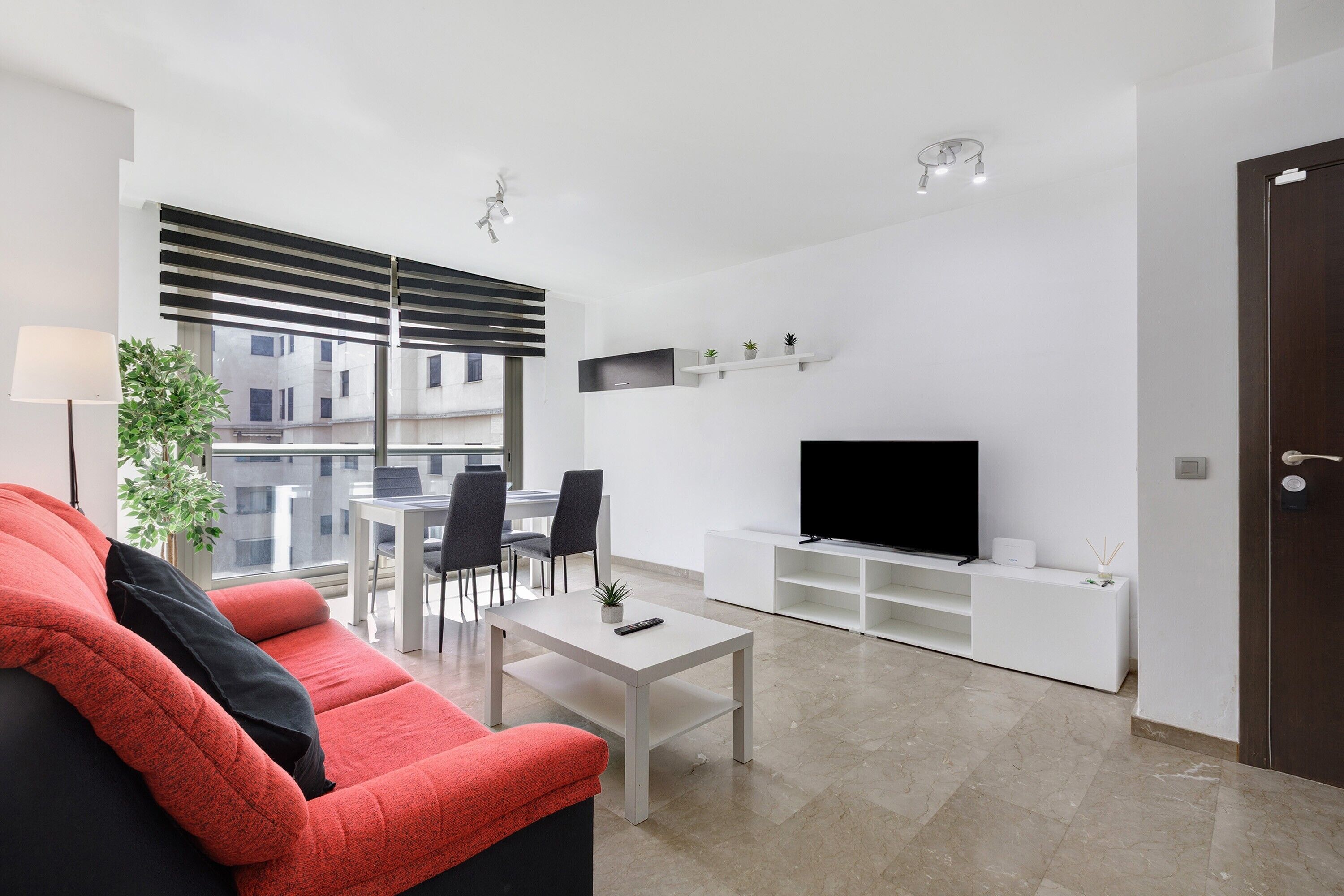 Una sala moderna con un sofá, una mesa de centro, un televisor y un comedor con sillas y una mesa.