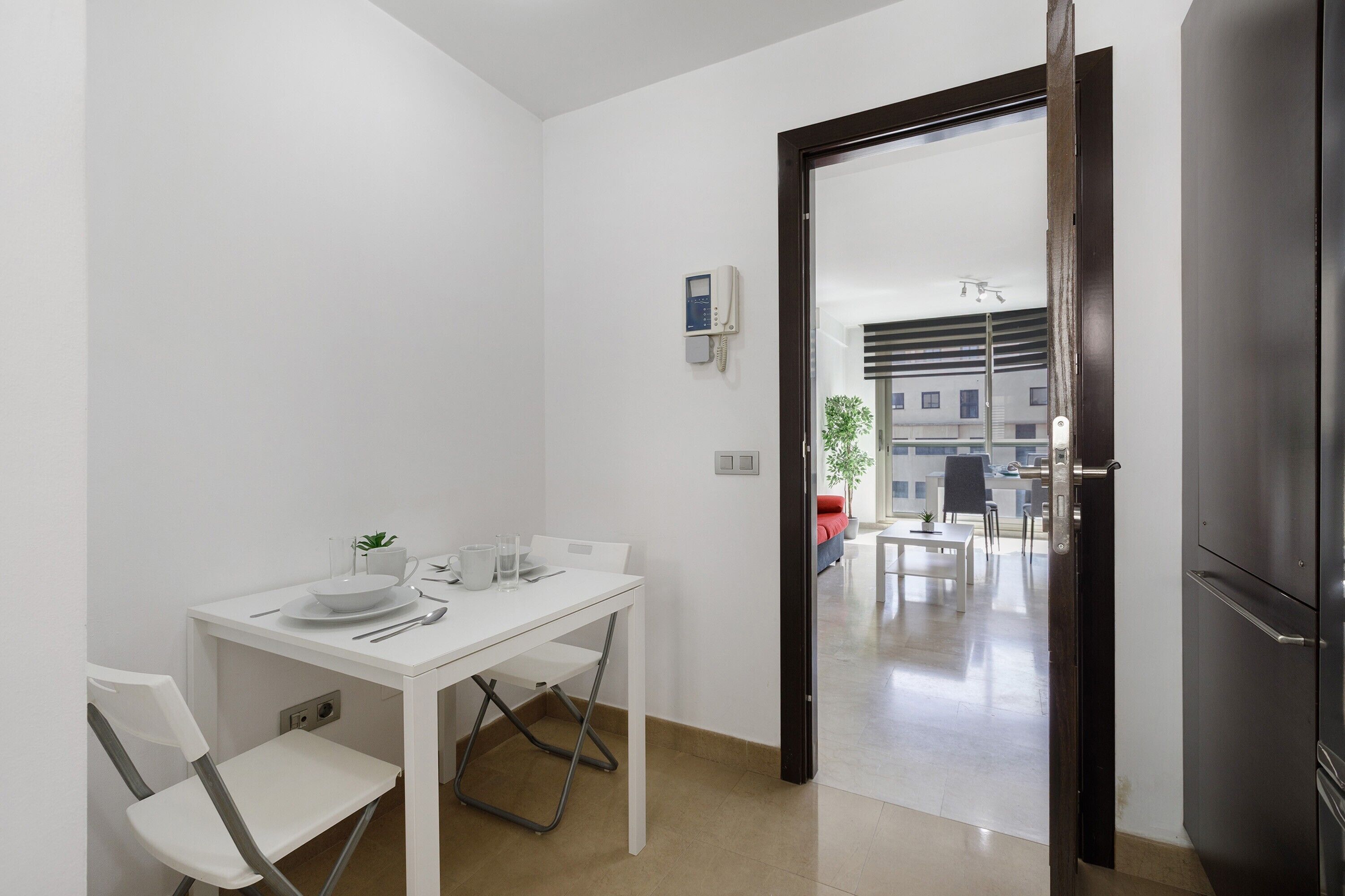 Cocina compacta con una mesa blanca para dos personas, una planta pequeña y un refrigerador moderno.
