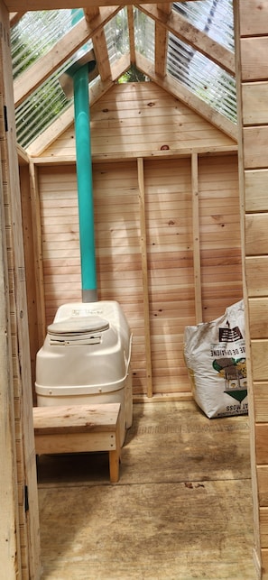Un intérieur en bois avec des toilettes, un tuyau vert et un sac d’engrais.