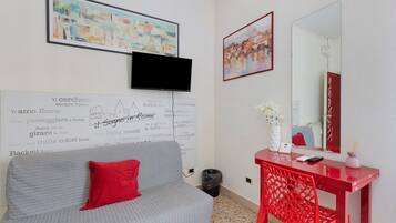 Habitación de hotel con un sofá gris, una almohada decorativa roja, un escritorio rojo con un espejo y obras de arte en las paredes.