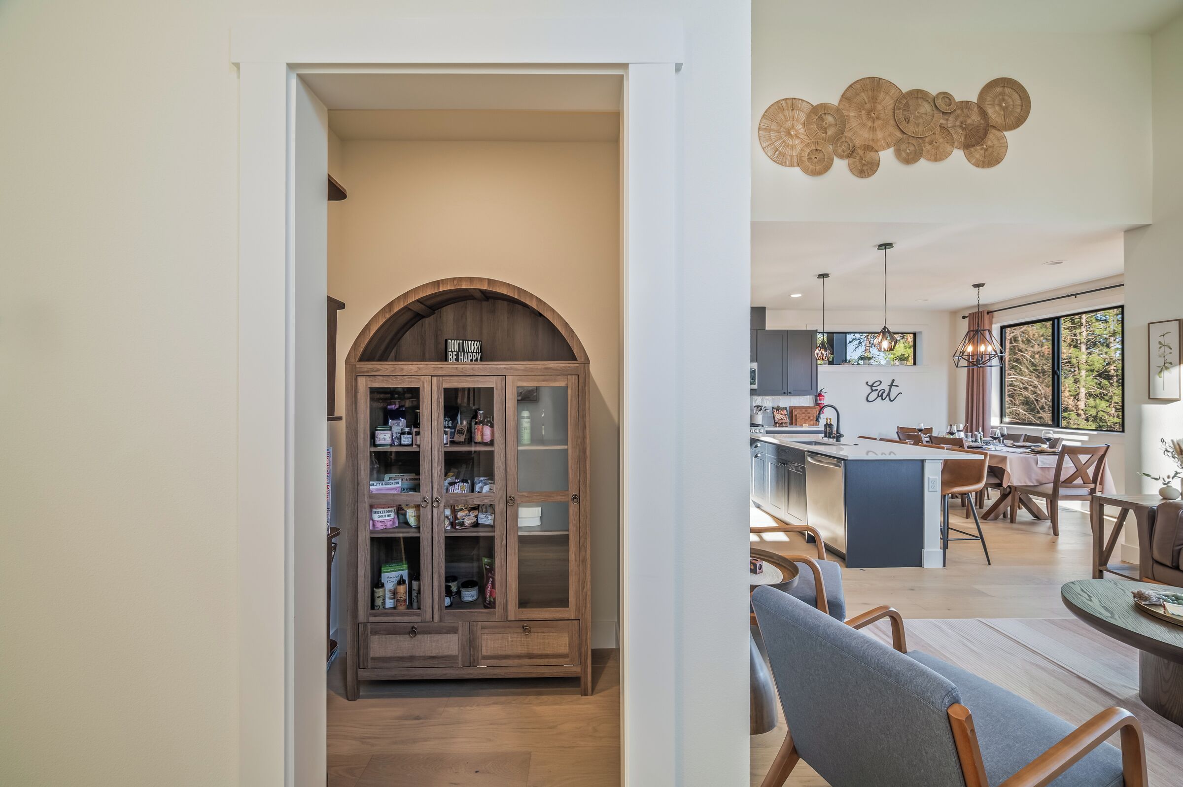A modern kitchen with a central island, dining area with chairs, and a wooden cabinet with glass doors.