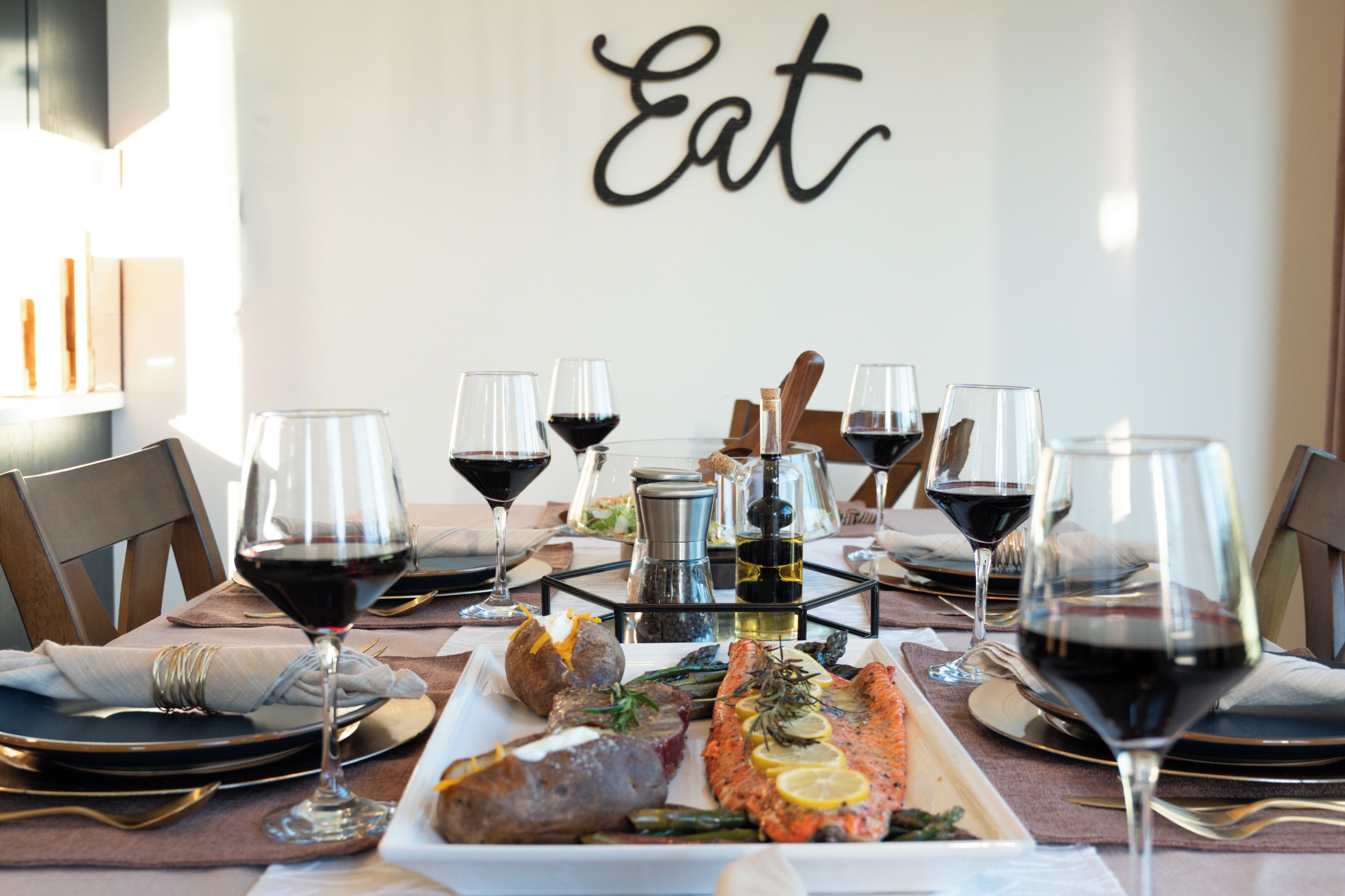 A dining table set with wine glasses, plates of food, and a bottle of olive oil.