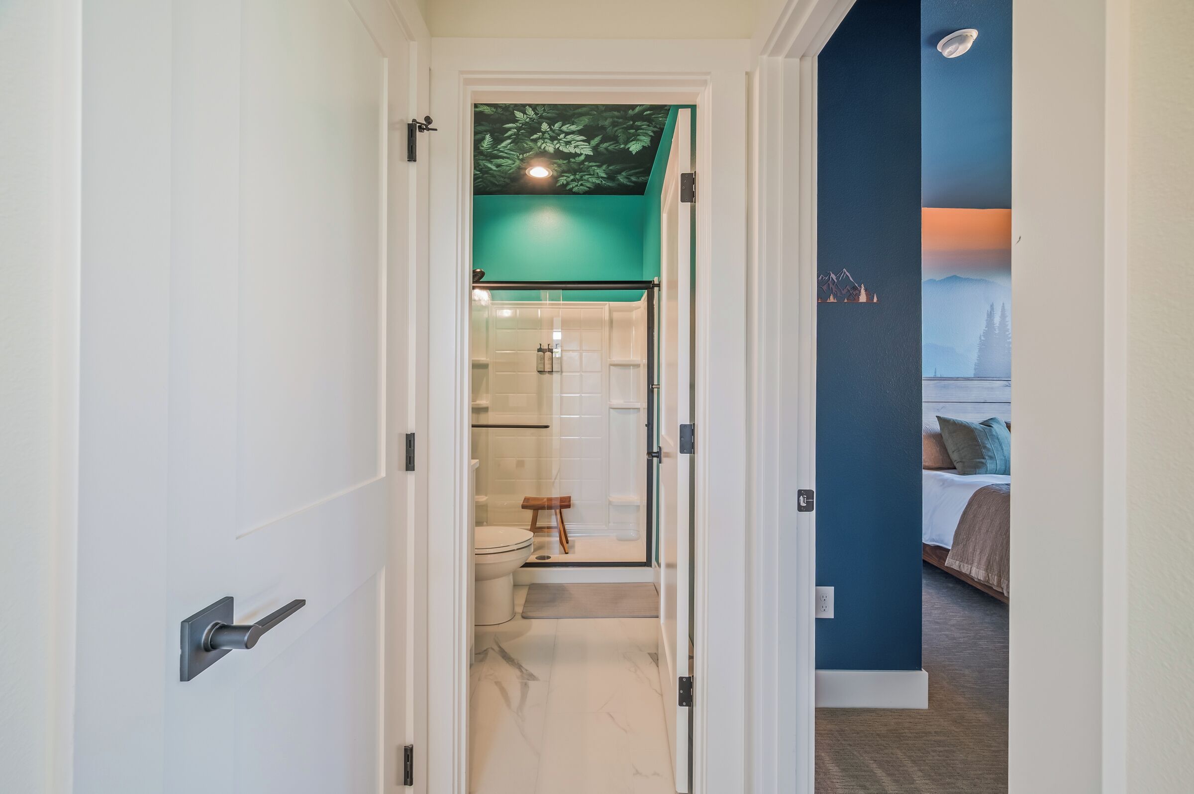 A hallway leading to a bathroom with a glass door, a shower, and a toilet.