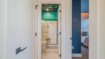 A hallway leading to a bathroom with a glass door, a shower, and a toilet.