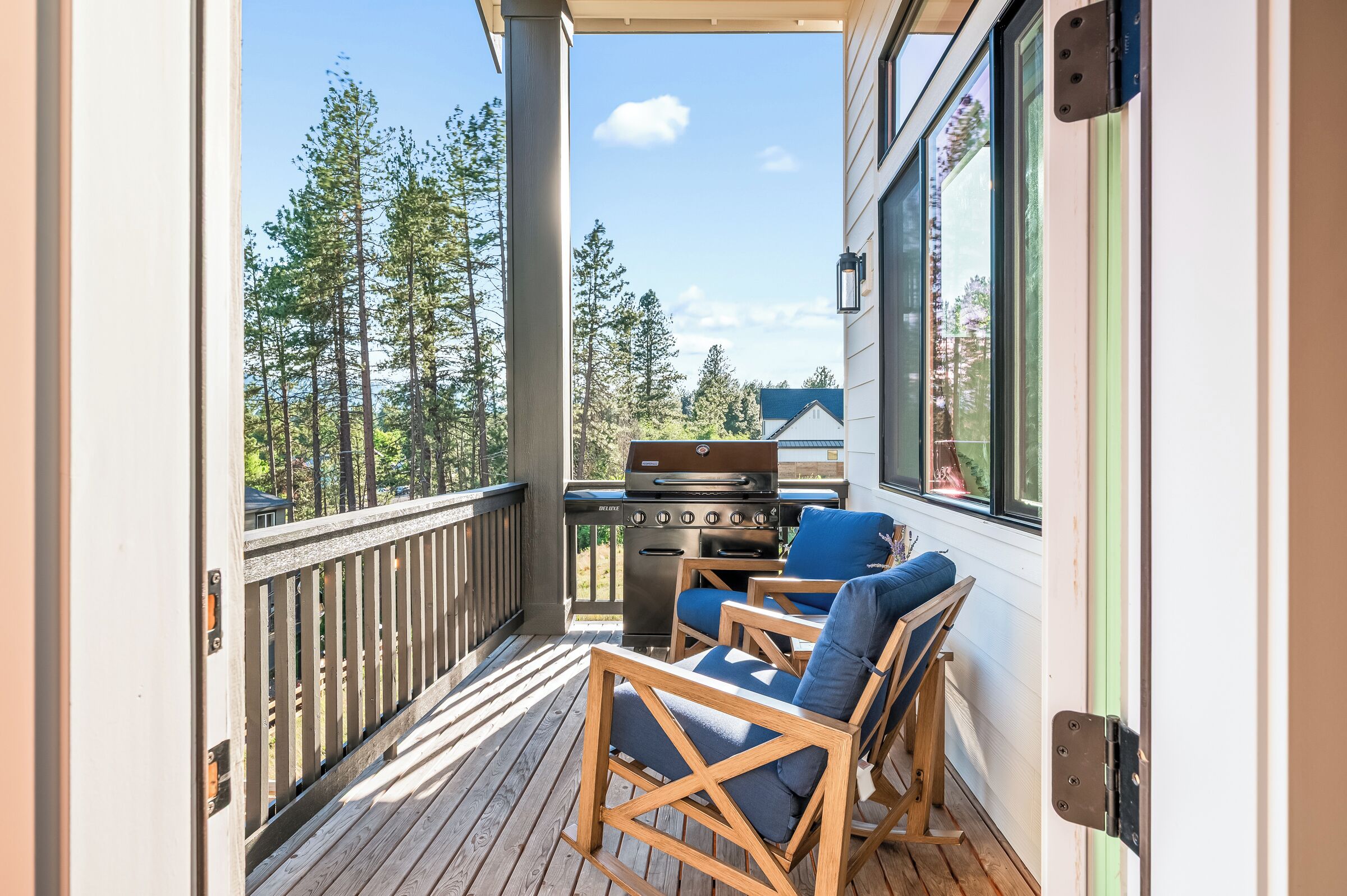 A deck with a grill, two chairs, and a view of trees.