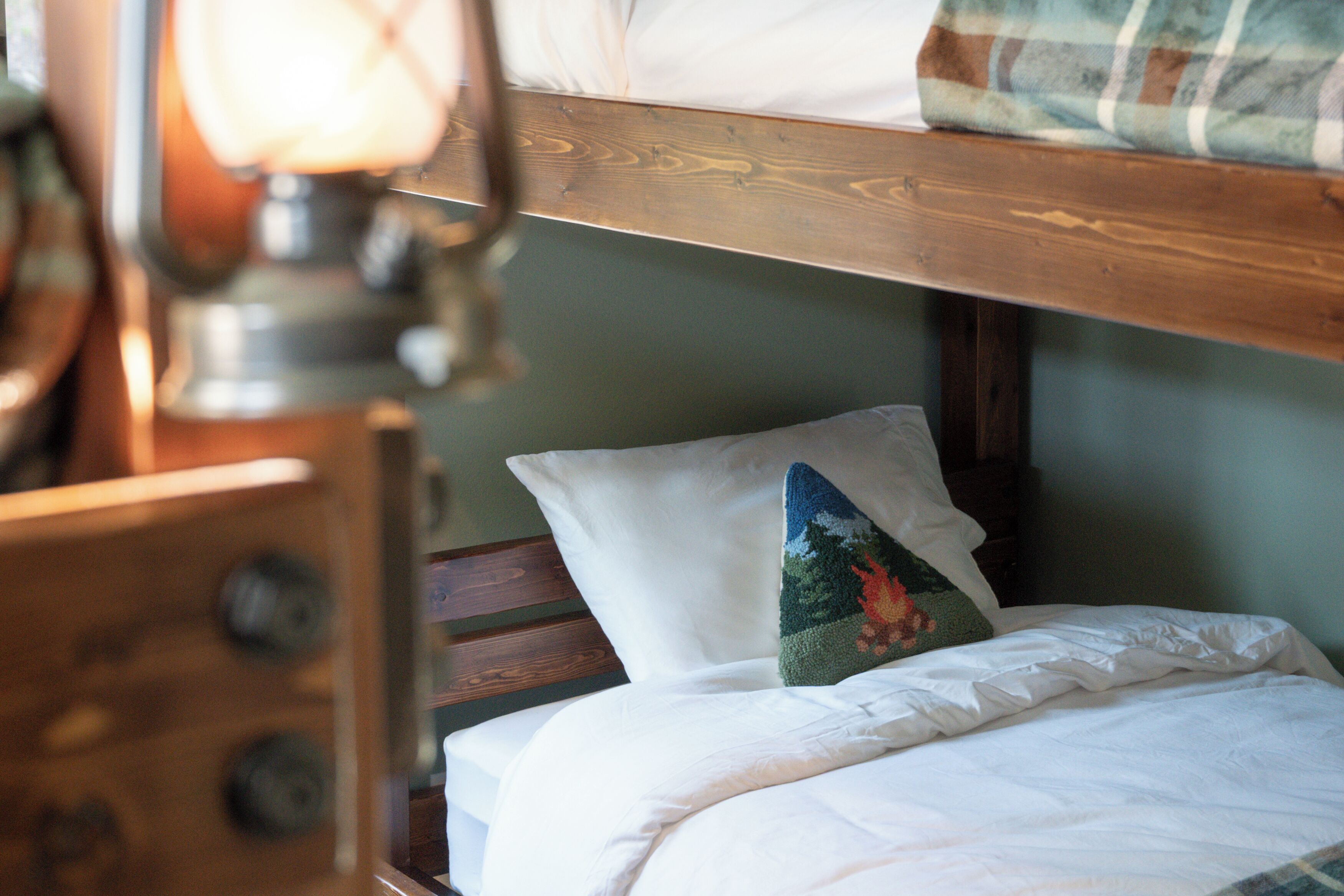 A bunk bed with a wooden headboard, a white pillow, and a decorative pillow with a nature scene.