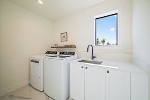 A laundry room with two washing machines, a sink, and a window with a view.