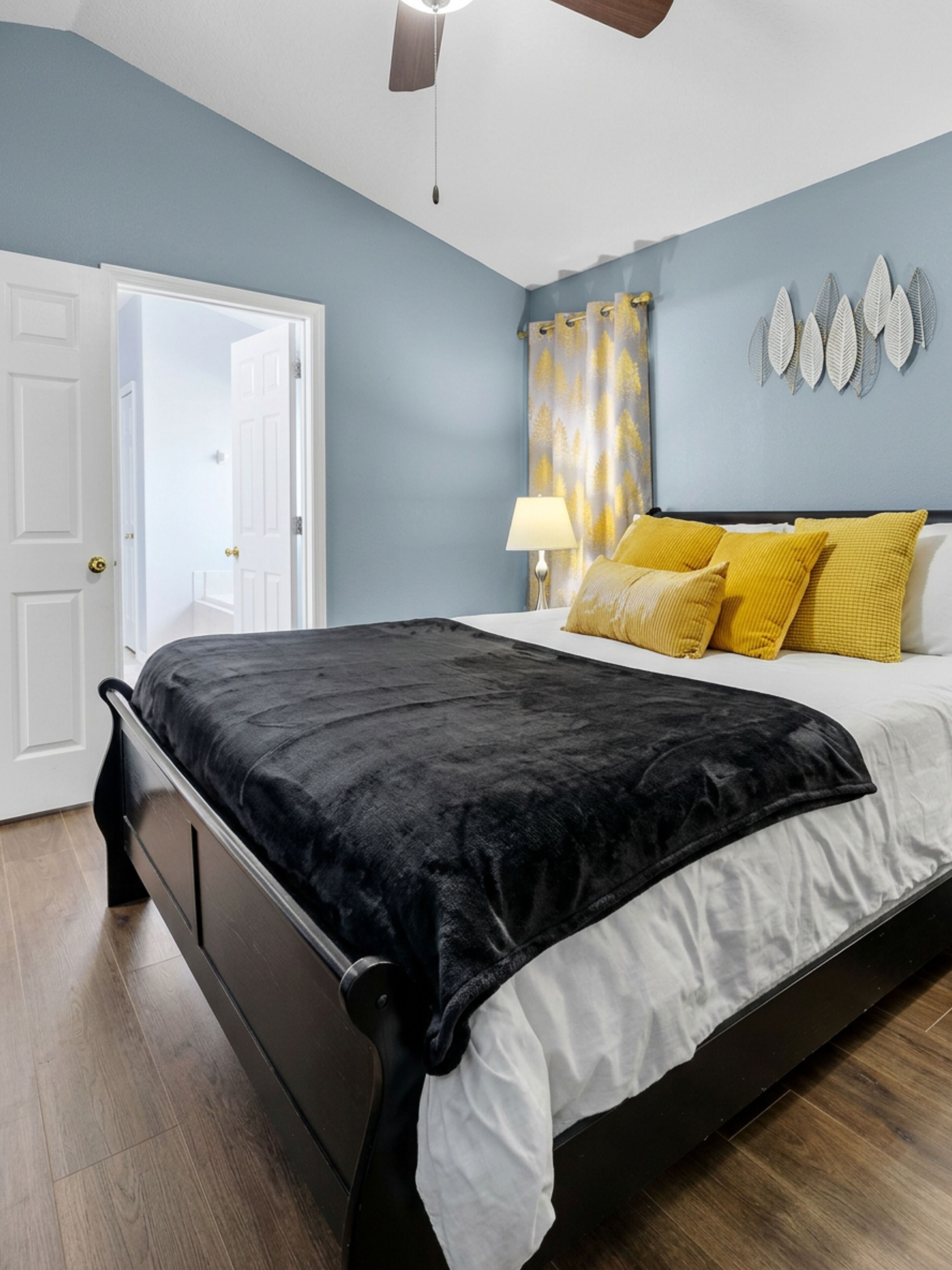 A bedroom with a bed, a door, a ceiling fan, and a wall with decorative elements.