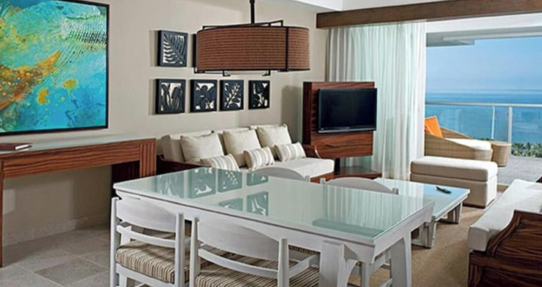 Une chambre d’hôtel moderne avec une table à manger en verre, un canapé, un téléviseur et des œuvres d’art accrochées au mur.