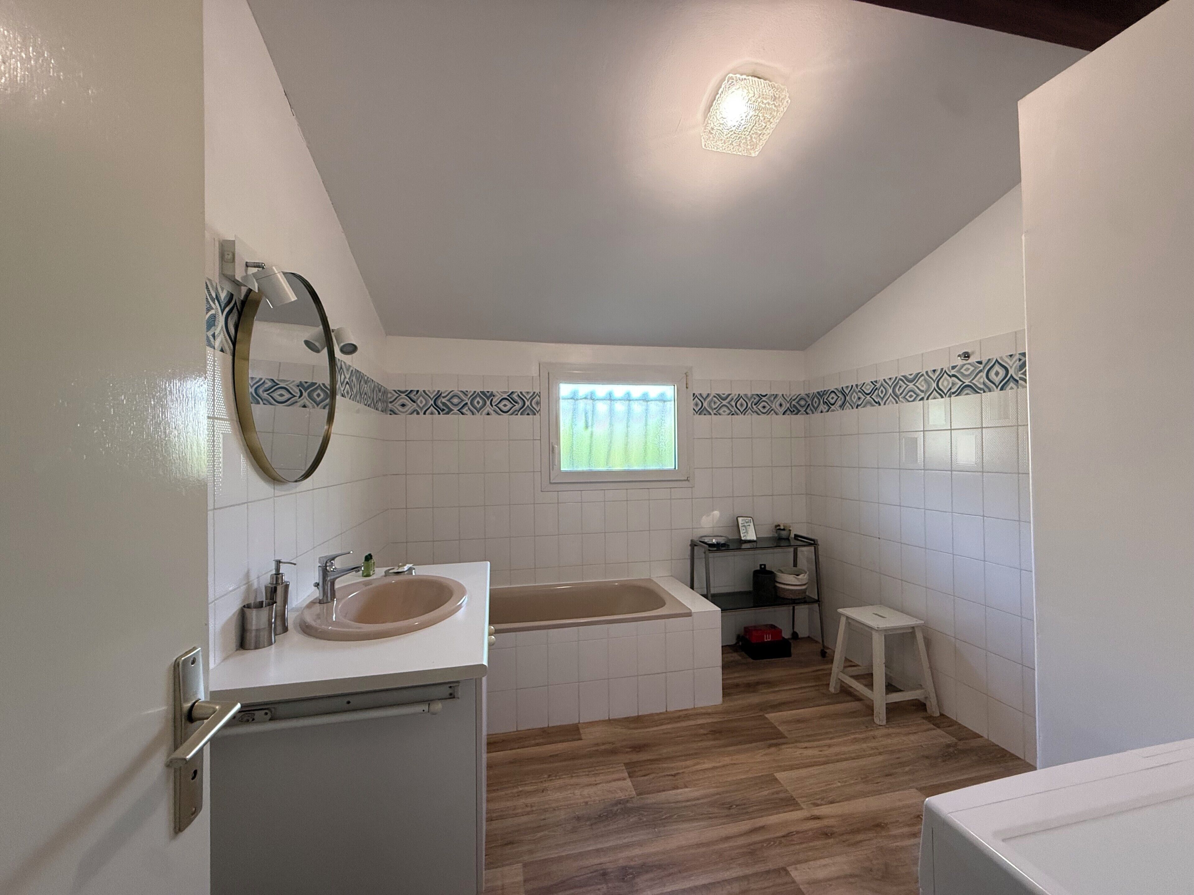 Une salle de bain avec un lavabo, un miroir, une baignoire et une fenêtre.