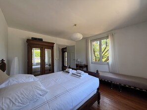 Ein Schlafzimmer mit einem großen Bett, einem Holzschrank, einem Nachttisch, einer Bank und einem Fenster mit Vorhängen.