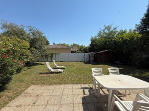 Ein Garten mit einer Terrassentischgruppe, einem Rasen und einem kleinen Schuppen.
