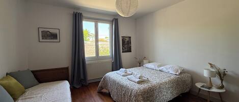 Een slaapkamer met twee bedden, een raam met gordijnen, een hanglamp en een klein nachtkastje met een lamp.