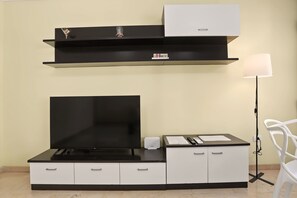 Un soggiorno moderno con una TV a schermo piatto, un mobile bianco, uno scaffale nero con oggetti decorativi e una lampada da terra.