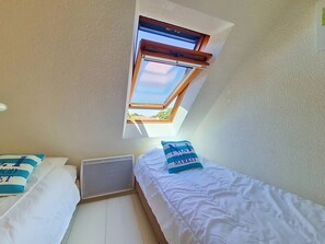 A room with two beds, a window, and a ceiling vent.