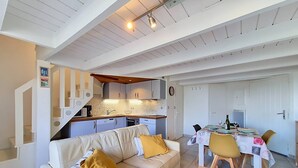 Una sala de estar moderna con un sofá, una mesa de comedor para dos personas y una zona de cocina con una escalera.