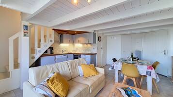 Un salon moderne avec un canapé, une table à manger pour deux personnes et un coin cuisine avec un escalier.