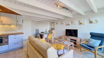 Un salon moderne comprenant un canapé, un téléviseur et un coin repas avec une table et des chaises.
