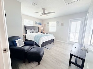 Ein Schlafzimmer mit einem Bett, einem Sessel, einem Schreibtisch, einem Deckenventilator und einer Tür.