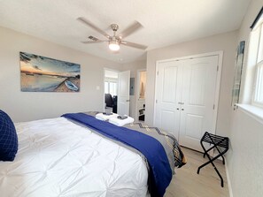 Ein Schlafzimmer mit einem Bett, einem Deckenventilator, einem Strandbild, einem Schrank und einem Fenster.
