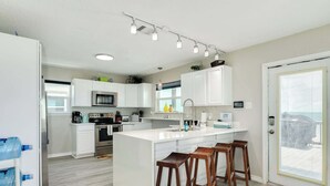 Una cocina moderna con armarios blancos, electrodomésticos de acero inoxidable y una isla central con taburetes de bar.