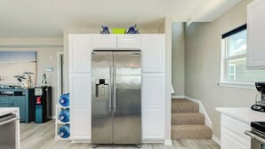 Una cocina moderna con un refrigerador de acero inoxidable, dispensadores de agua y una cafetera sobre la encimera.