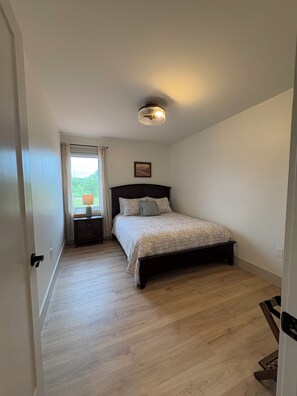 A bedroom with a bed, a nightstand, a lamp, a ceiling light, and a window with curtains.