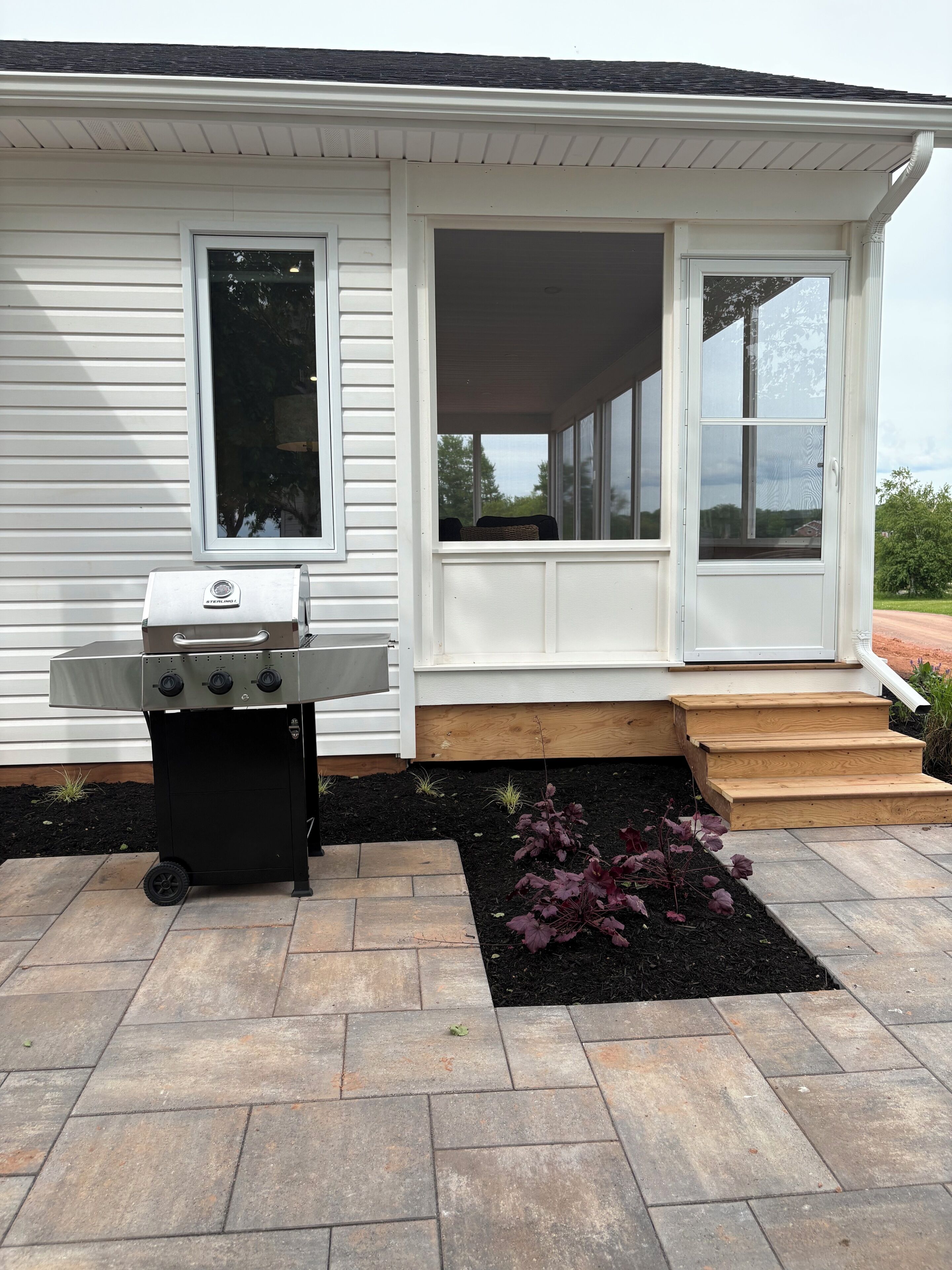 A house with a covered porch, a grill, and a small garden with stepping stones.