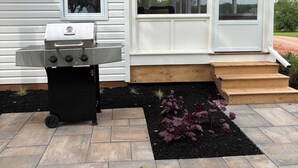 Uma casa com varanda coberta, churrasqueira e um pequeno jardim com pedras para caminhar.