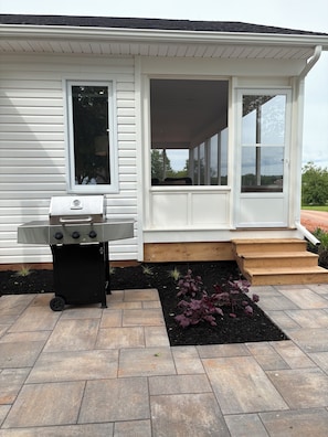 A house with a covered porch, a grill, and a small garden with stepping stones.