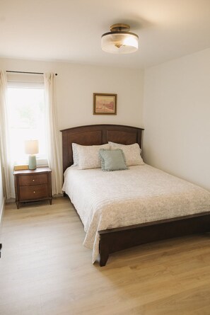 A bedroom with a wooden bed, a nightstand, a lamp, and a ceiling light fixture. - Brand New Cottage in Stratford-Hot Tub, incredible water view! (Stratford)