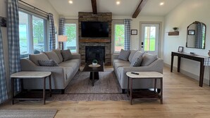 A spacious living room with a stone fireplace, two sofas, a coffee table, and a TV mounted on the wall.