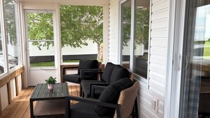 A covered porch with a table and chairs, a woven chair, and a view of the outdoors.