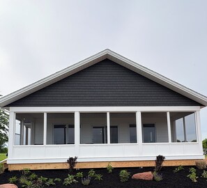 A single-story house with a dark roof, white exterior walls, and a covered porch with multiple windows. - Brand New Cottage in Stratford-Hot Tub, incredible water view! (Stratford)