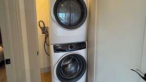 Uma lavanderia com duas máquinas de lavar de abertura frontal, uma porta que dá para outro espaço e uma tomada visível.