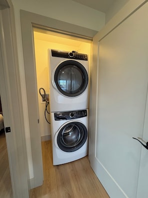 A laundry room with two front-loading washing machines, a door leading to another room, and a visible electrical outlet.