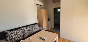 A room with a sofa, a small table, a remote control, and a wooden cabinet.
